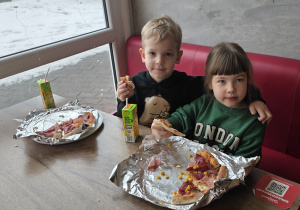 Dzieci jedzą wspólnie pizzę.