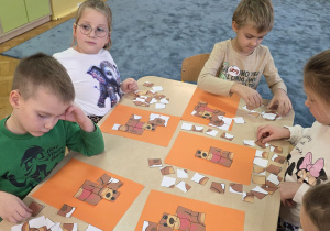 Dzieci pracują przy stolikach - układają wizerunek misia z pociętych elementów (puzzli).