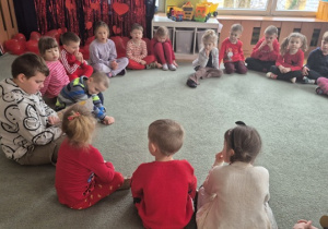 Dzieci siedzą na dywanie i słuchają czytanego opowiadania.