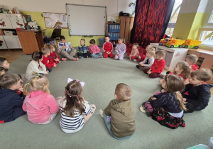 Dzieci siedzą na dywanie i słucha opowiadania czytanego przez Kacpra.