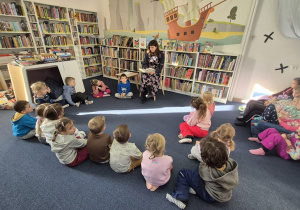 Dzieci siedzą na dywanie i słuchają opowiadania.