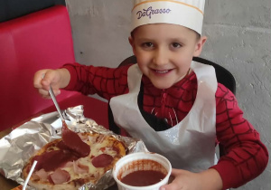 Chłopiec nakłada sos pomidorowy na pizzę.