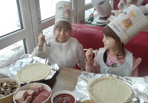 Dziewczynki trzymają łyżki, by móc nałożyć sos na pizzę.