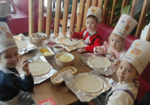 Dzieci trzymają łyżki, by móc nałożyć sos na pizzę.