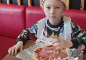 Chłopiec nakłada składniki na pizzę.