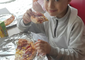 Dziewczynka i chłopiec jedzą pizzę.