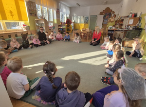 Dzieci siedzą na dywanie i czekają na rozpoczęcie zajęć.