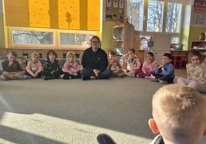 Dzieci siedzą na dywanie i witają się z Panią Kasią i Panem Igorem.