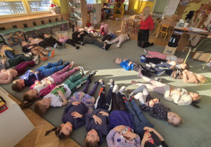 Dzieci leżą na dywanie i sprawdzają jak pracuje ich przepona.