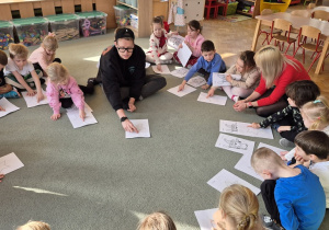Dzieci siedzą na dywanie i ćwiczą wspólnie z Panią Kasią i Panem Igorem wdech i wydech.