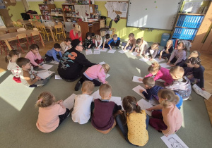 Dzieci siedzą na dywanie i ćwiczą prawidłowe oddychanie.
