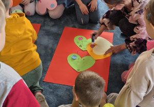 Dzieci przyklejają wykonane serca na duży karton i tworzą radosny plakat.