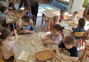 Dzieci wycinają w masie plastycznej dinozaury, odciskają szkielety dinozaurów.