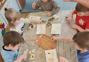 Dzieci ozdabiają dinozaury makaronem w różnym kształcie.