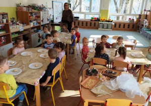 Dzieci siedzą za stolikami, na których ustawione są talerzyki z kulami wykonanymi z sody.