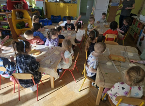 Dzieci siedzą przy stolikach i słuchają co mają ronić