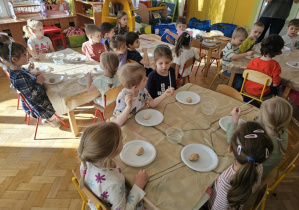 Dzieci siedzą za stolikami, na których ustawione są talerzyki z kulami wykonanymi z sody.