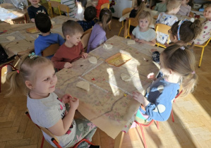 Dzieci siedzą przy stolikach i rozwałkowują swoją masę solną.