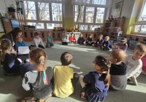 Dzieci siedzą na dywanie a Pani Ola czyta opowiadanie.