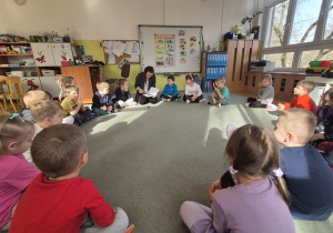 Dzieci siedzą i słuchają czytanego opowiadania.