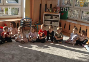 Dzieci siedzą na dywanie w półkolu- czekają na gości.
