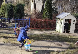 Dziecko zbiera do wiaderka rozrzucone przez siebie wcześniej kolorowe piłeczki.