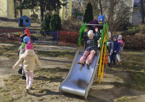 Dzieci kolejno zjeżdżają na zjeżdżalni.