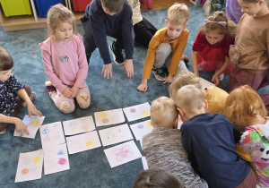 Dzieci tworzą na dywanie wystawę prac.