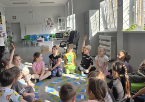 Dzieci rozwiązują zagadki słowne. Podnoszą ręce do góry, jeśli chcą odpowiedzieć.