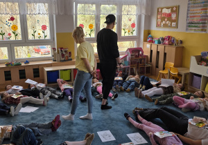 Dzieci leżą na dywanie i trzymają książki na swoich brzuszkach. Sprawdzają, co dzieje się z ciałem podczas oddychania.