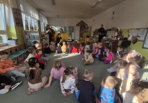 Dzieci siedzą na dywanie i słuchają opowiadania.