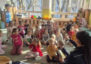 Dzieci siedzą na dywanie i słuchają czytanego opowiadania.