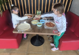 Dzieci siedzą i tworzą swoje Pizze.