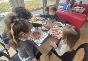 Dzieci nakładają na przygotowane ciasto szynkę i salami.