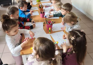 Dzieci stoją przy stolikach i działają twórczo.