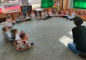 Dzieci siedzą na dywanie w kole i odpowiadają na pytania pani Kasi.