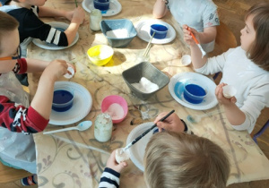 Dzieci smarują skorupki jaj klejem przed włożeniem do solanki.