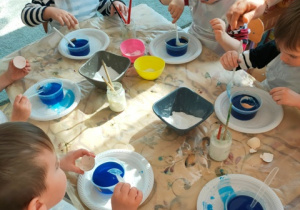 Dzieci umieszczają skorupki jaj w pojemnikach z zabarwioną solanką.