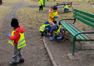 Dzieci zbierają śmieci wokół ławeczki.