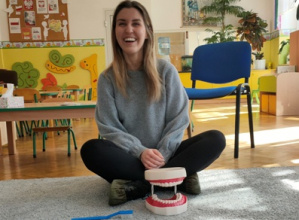 Pani stomatolog siedzi na dywanie, przed nią leży model szczęki dentystycznej i szczoteczka.