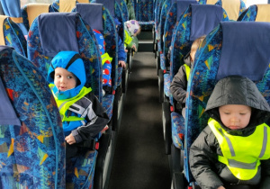 Dzieci siedzą w busie, zapięte pasami - czekają na odjazd spod przedszkola.