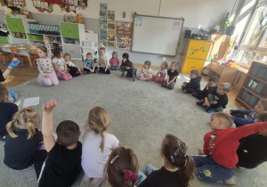 Dzieci siedzą na dywanie i odpowiadają na pytania Pani Kasi.