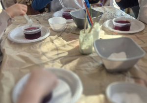 Dzieci umieszczają skorupki jajek wysmarowane klejem w pojemnikach z zabarwioną solanką.