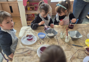 Dzieci umieszczają skorupki jajek wysmarowane klejem w pojemnikach z zabarwioną solanką.