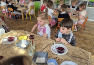 Dzieci umieszczają skorupki jajek wysmarowane klejem w pojemnikach z zabarwioną solanką.