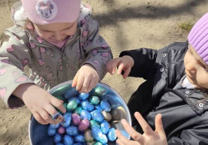 Dziewczynki przynoszą kolejne znalezione kolorowe jajeczka.