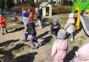 Dzieci szukają w ogrodzie przedszkolnym ukrytych jajeczek wielkanocnych.