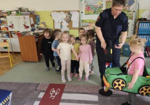 Piesi- grupa dzieci- czekają na zmianę koloru światła, by móc przejść na drugą stronę ulicy.