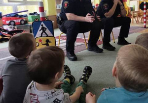 Dzieci siedzą na dywanie, odpowiadają na pytania zadawane przez przedstawicieli Straży Miejskiej.