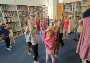 Dzieci bawią się z panią bibliotekarką wykonując zadania ruchowe.